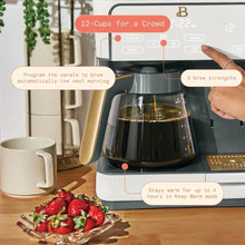 White coffee maker with glass carafe filled during brewing, control panel visible