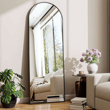 Black arched full-length floor mirror with slim frame, leaning in entry room