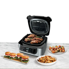 Electric indoor grill with open lid and basket holding grilled meat