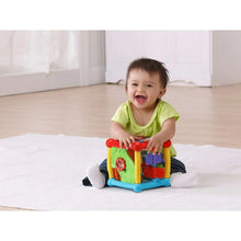 Infant playing with a colorful plastic activity cube toy with red top button tiles