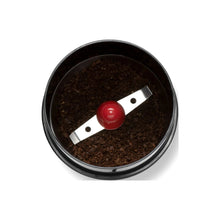 Electric coffee grinder grinding chamber with dark coffee grounds, metal blade and red cap
