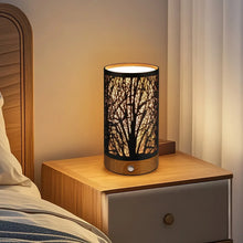 Table lamp with black cylindrical shade and wooden base, lit on a nightstand.