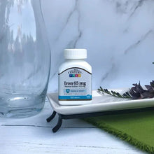 Iron 65 mg supplement bottle on tabletop with plant and glass
