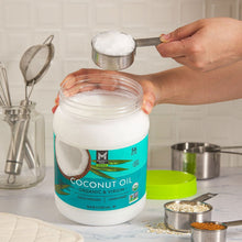 Person scooping white coconut oil from a jar with green-capped lid