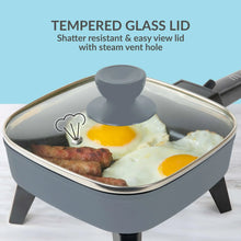 Gray electric skillet with tempered glass lid and steam vent, cooking eggs and sausage