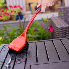 Hand holding red scrub brush with black bristles for outdoor surface cleaning