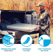 Gray folding table on outdoor ground with black frame; tabletop being positioned by handle.