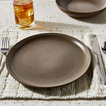 Brown stoneware dinner plate with speckled glaze, on table with drink and utensils