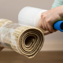 Hand applying clear stretch wrap over rolled item, visible plastic stretch film