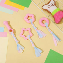 Pink rubber dog chew toys with braided rope handles and tassels, arranged on a tile surface