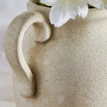 Beige speckled ceramic jug vase with loop handle, topped with white artificial flowers