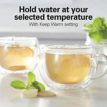 Electric glass kettle with black handle next to two glass cups of tea