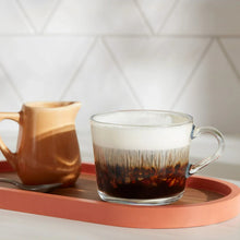 Glass mug of dark coffee with crema and a small carafe on a serving tray