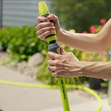 Person holding lime-green spray nozzle on a garden hose to water plants
