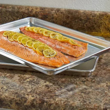 Half-size aluminum sheet pan with baked salmon on a countertop