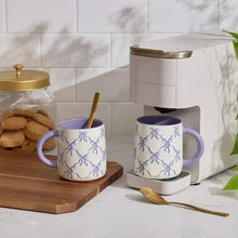 Pair of purple-lined white stoneware mugs with blue bow motif and lavender handles