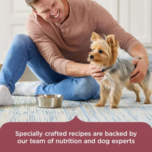 Man petting a small dog while holding a bowl of dry dog food
