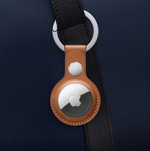 Apple AirTag tracker on a brown leather key fob attached to a black strap