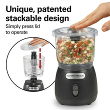 Black food chopper with clear lid and stacked top, showing press operation