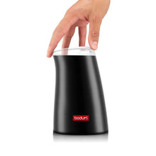 Electric coffee grinder in black with open transparent hopper lid held by hand