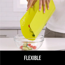 Yellow flexible plastic cutting mat being lifted above a bowl of chopped produce