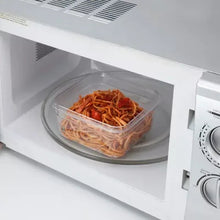 Clear plastic food container with black lid, containing cooked spaghetti in microwave