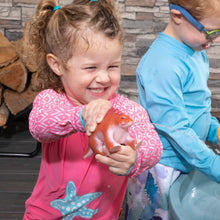 Toddler holding orange dinosaur toy near blue dino water table basin