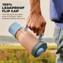 Personal blender travel cup with flip cap in hand, dark gray base and blue lid.