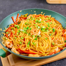 Green nonstick fry pan filled with noodles, shrimp, and vegetables