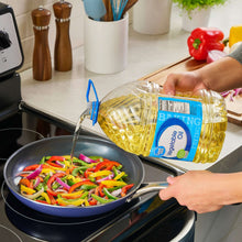 Vegetable oil jug with blue handle being poured into a skillet of mixed vegetables.