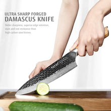 Damascus chef knife held in hand, dark textured blade with light wooden handle