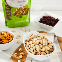 Roasted pistachios in shell with kernels in white bowls and a green pistachios bag