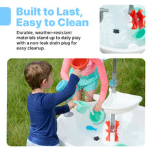 Child rinsing colorful splash toys on an outdoor water table with umbrella canopy