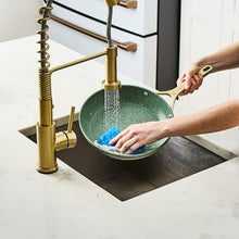 Olive non-stick frying pan being cleaned, with long handle and speckled interior