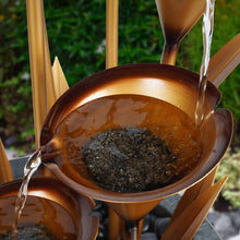 Copper basin fountain with bubbling water over dark stones