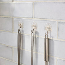 Three clear suction cup hooks mounted on a tiled wall with metal hooks