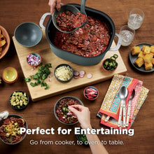 Sage green multi-cooker on wooden board with small bowls and plates