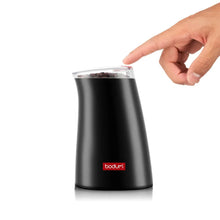 Electric coffee grinder in black with transparent hopper; hand adjusting the lid