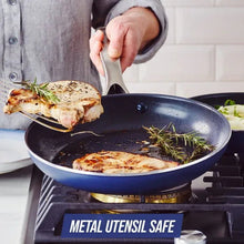 Dark blue ceramic nonstick skillet with long metal handle, food cooking inside