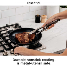 Black nonstick frying pan with stainless handles, holding seared meat on stove burner