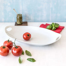 White oval porcelain tray with side handles holding tomatoes and basil