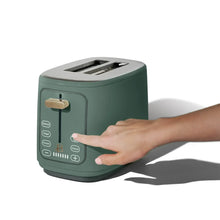 Dark green 2-slice toaster with a hand touching the front touch controls