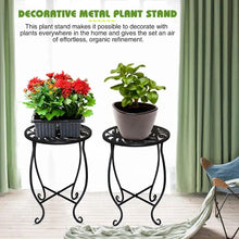 Black round metal plant stand with perforated top and scroll legs, supporting a potted plant.