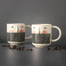 Two stoneware mugs with cheeky faces, cream glaze, black polka-dot band, side handles