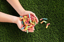 Hand holding colorful gummy candy worms on green grass