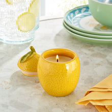 Yellow ceramic lemon fruit candle with lit wick on tabletop