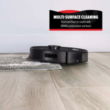 Black robot vacuum with cleaning pad on light wood floor tile