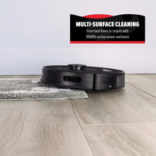 Black robot vacuum cleaning on hardwood floor beside a rug