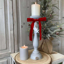 Red velvet Christmas bow with long tails, centered over a white display stand.