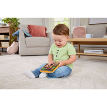 Baby sitting on floor holding an orange learning tablet toy with colorful icon buttons